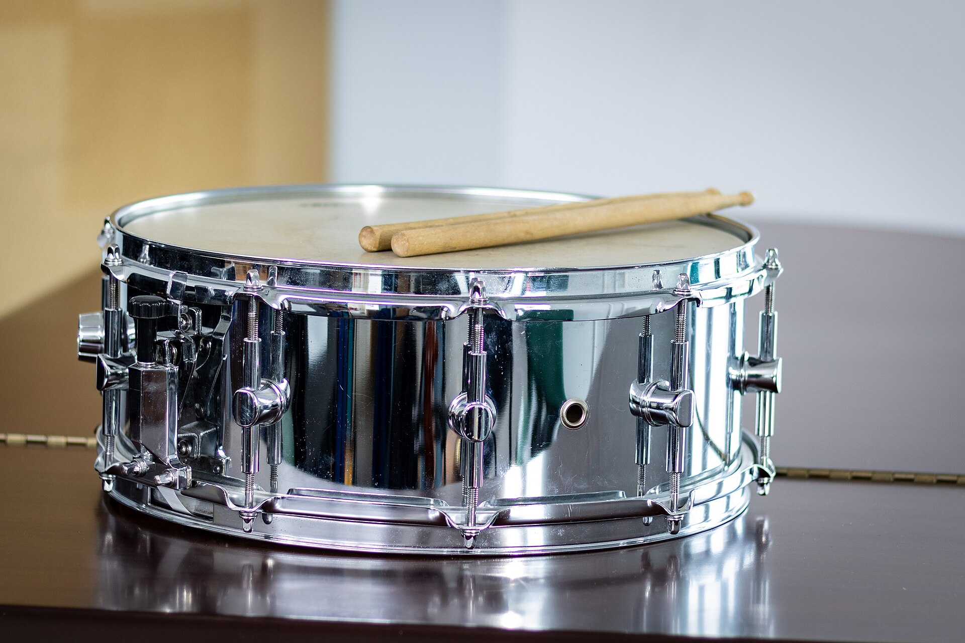 A snare drum with two drumsticks resting on its head